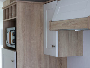 Laagpolig: moderne keuken in een stacaravan aan zee met houtafwerking en wit kastwerk, perfect voor een comfortabele en stijlvolle vakantie ervaring.