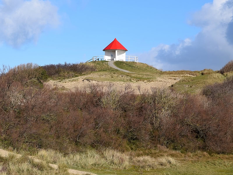Uitzicht op zee en natuur met een kleine witte bungalow met rood dak op een duin.