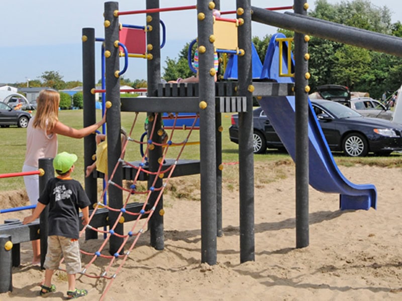 Veilig speeltoestel op het strand met zand en kinderen die spelen, ideale locatie voor families die een stacaravan aan zee boeken.