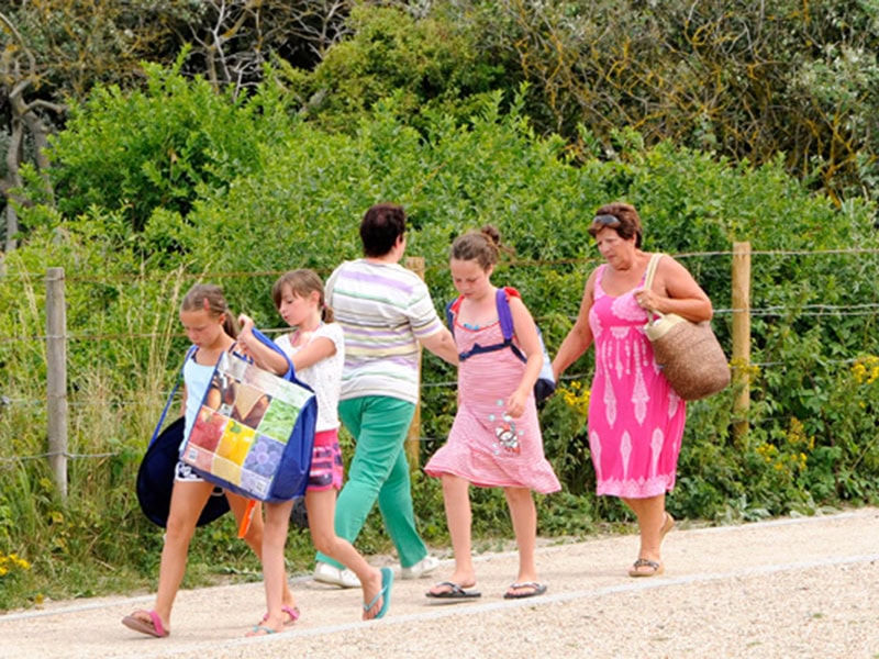 Gezinnetje wandelen in de natuur bij een stacaravan aan zee, zomervakantie, kids en volwassenen genieten van de buitenlucht en de zee op de achtergrond.