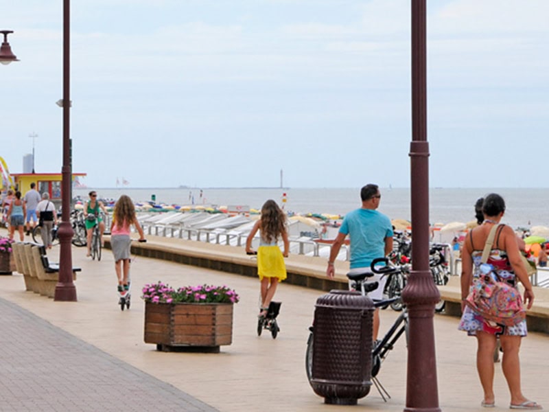 Gezellig strandwandelen aan de zee met gezinnen en fietsers onder de parasols en blauw water naar de charmante stacaravan op de Belgische kust.
