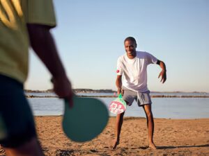 Stacaravan aan zee Gezicht op een man die beachvolleybal speelt op het strand bij zee, met een andere speler in de voorgrond. Perfect voor een vakantie aan zee met comfortabele stacaravans.